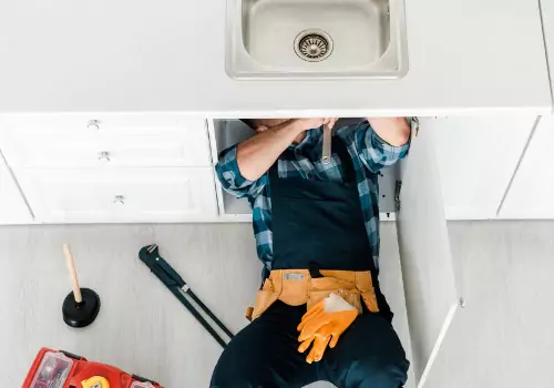 A plumber is seen working under a sink. Reading Plumbing is a 24 Hour Plumber in Washington IL.