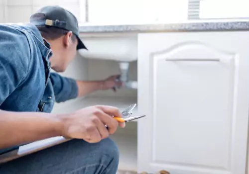 A plumber is seen working under a sink. Reading Plumbing offers plumbing services near you.