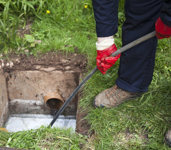Sewer Cleaning Peoria IL, Drain being cleared by worker in navy overalls.