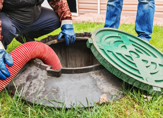 Sewer Cleaning Peoria IL, Maintenance of rural sewerage systems, pumping out wastewater using a submersible sewage pump.Pipe in a drain hole, servicing a septic tank in a backyard, removing waste with a hose and ensuring proper maintenance.